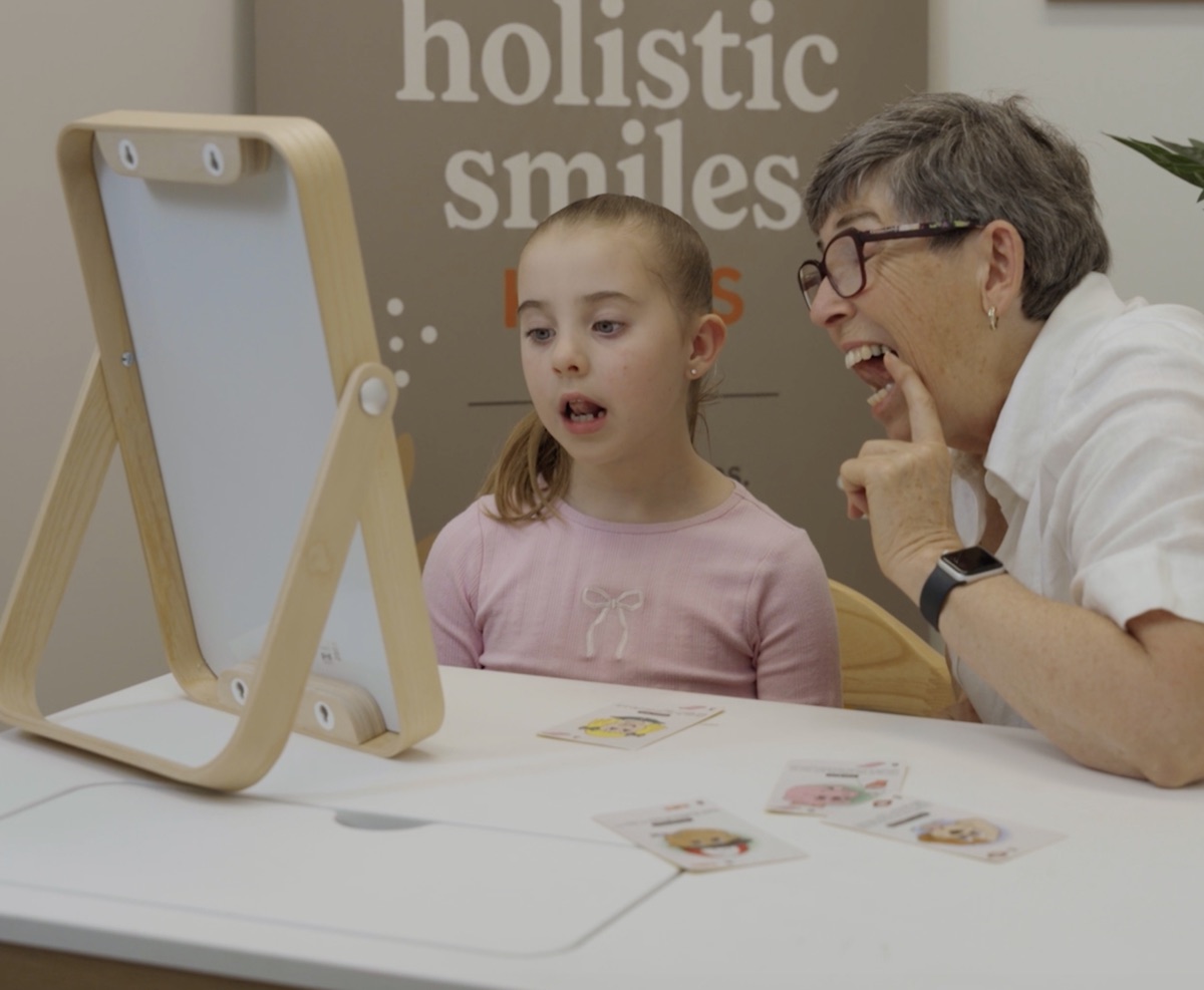 A myology educator guiding a child through a mirror exercise at Holistic Smiles Kids